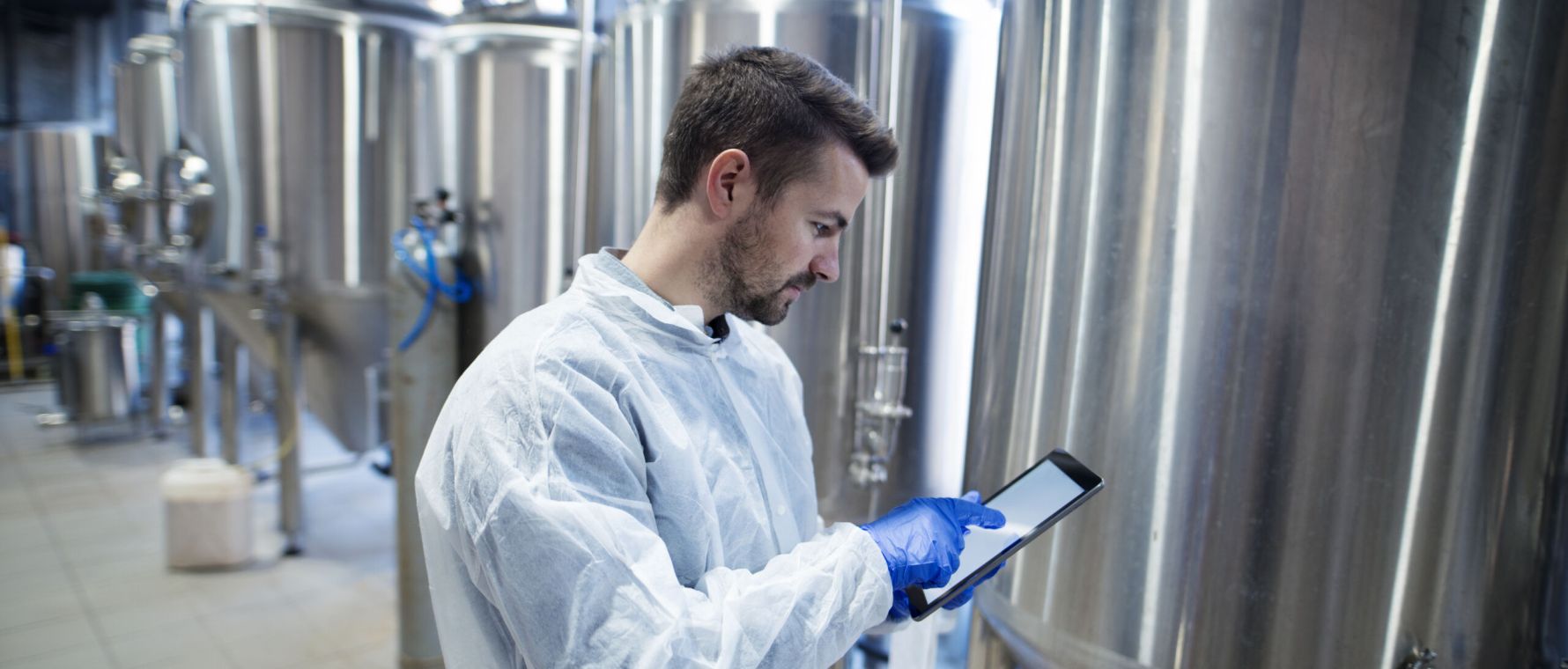 Technologist expert standing in food production plant and typing on his tablet computer.