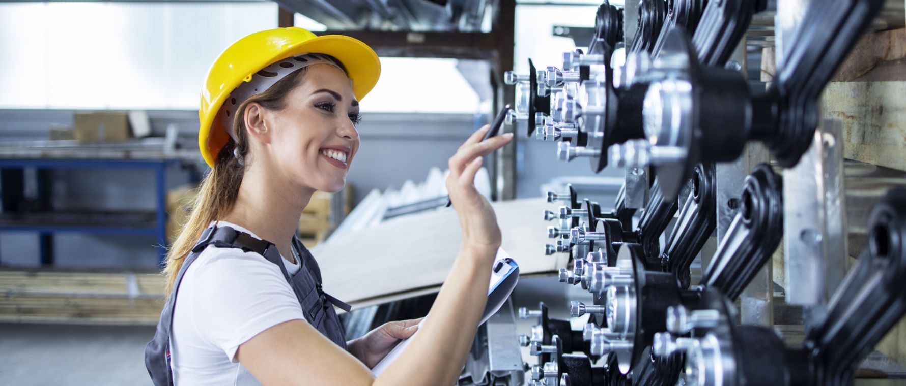 Woman industrial employee in working uniform and hardhat checking production in factory.